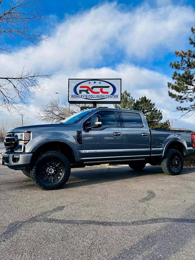 A gray Ford Super Duty pickup parked in front of the Rowley's Collision Center sign in Loveland